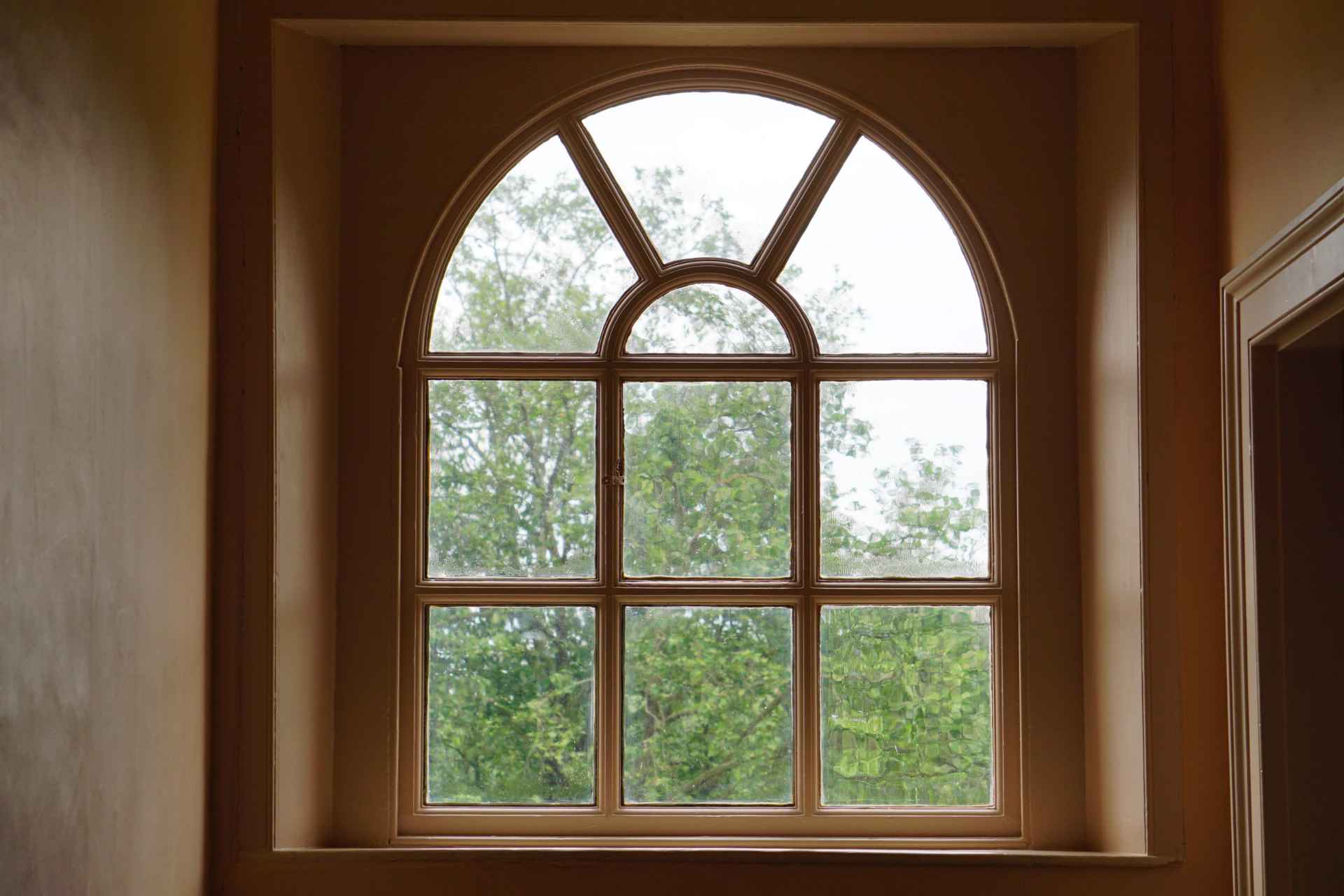 Interior view looking through a beige arched window with focus on frame details and potential hidden window damage.